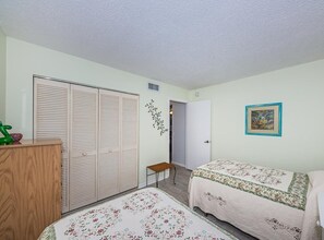 A bedroom with two beds, a wardrobe, a small table, and a door leading to another room.