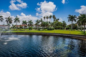 A water feature with a fountain, surrounded by a well-maintained lawn and palm trees, under a clear blue sky.