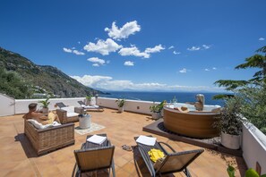 Une terrasse sur le toit, aménagée avec des meubles en osier, un jacuzzi et des plantes en pot.