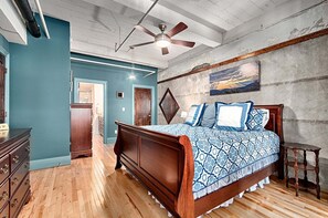 A bedroom with a wooden bed, a ceiling fan, and a painting on the wall.