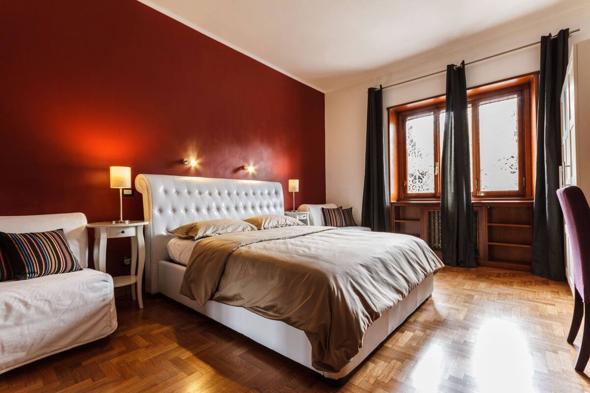 A bedroom with a large bed, two bedside tables, a chair, and a window with curtains.