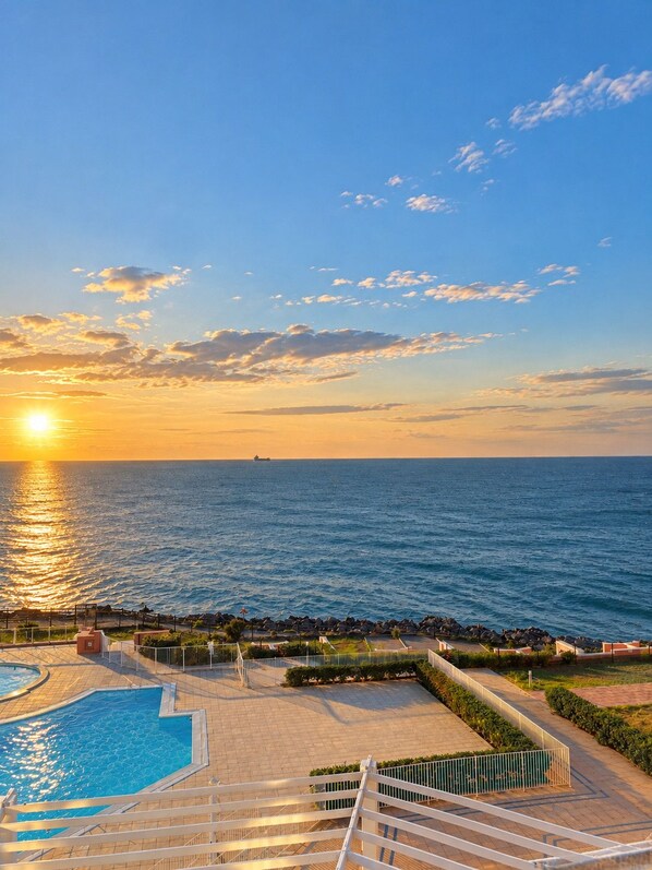 A pool area with a view of the ocean and a sunset.