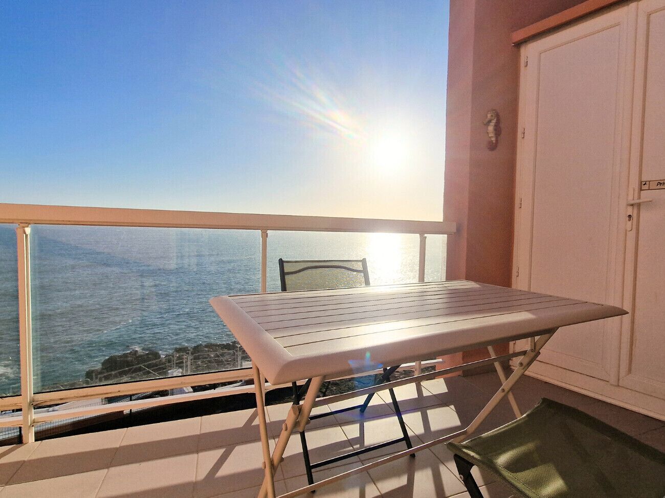 A balcony with a table and chair, overlooking a coastal view.
