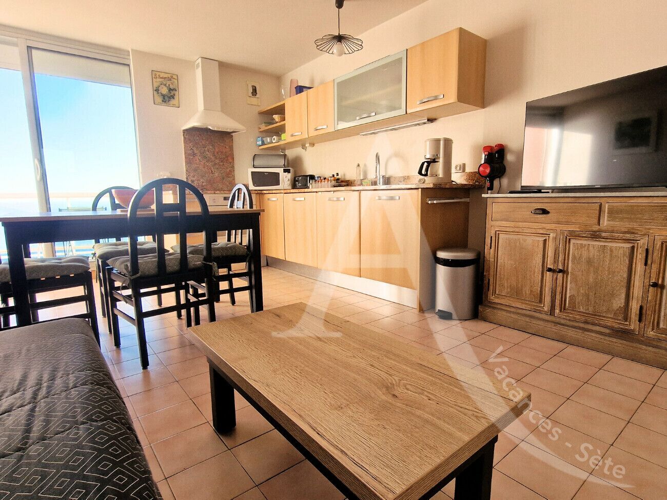 A modern kitchen with wooden cabinets, a dining table with chairs, and a large window providing a view of the outdoors.