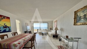 Amplia sala de estar con comedor, sofá, mesa de centro y vista al mar a través de amplias ventanas.