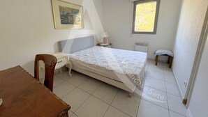 Un dormitorio pequeño con una cama individual, una silla, una mesa y una ventana.