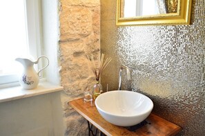 A bathroom with a stone wall, a white sink, a gold-framed mirror, and a wooden shelf with a white pitcher and reed diffusers. - Lux Green Garden in top Split Neighbourhood (Split)