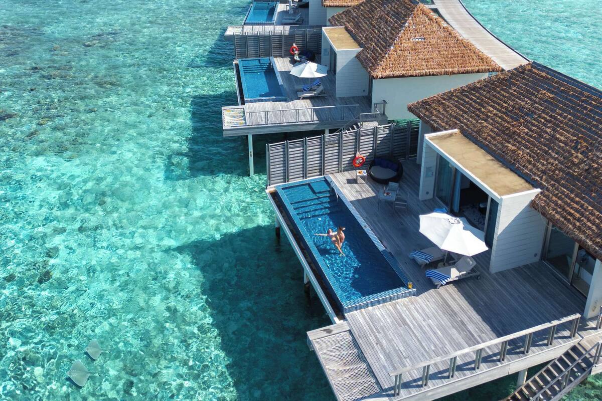 Cabañas sobre el agua con piscinas infinitas, agua turquesa cristalina y vistas al océano.
