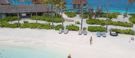 A beach resort with clear turquoise waters, palm trees, and overwater bungalows.
