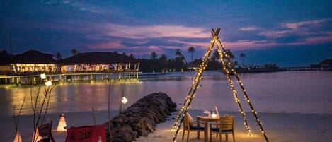 A beach setup with a bicycle, a table with chairs, and a tent-like structure adorned with lights.