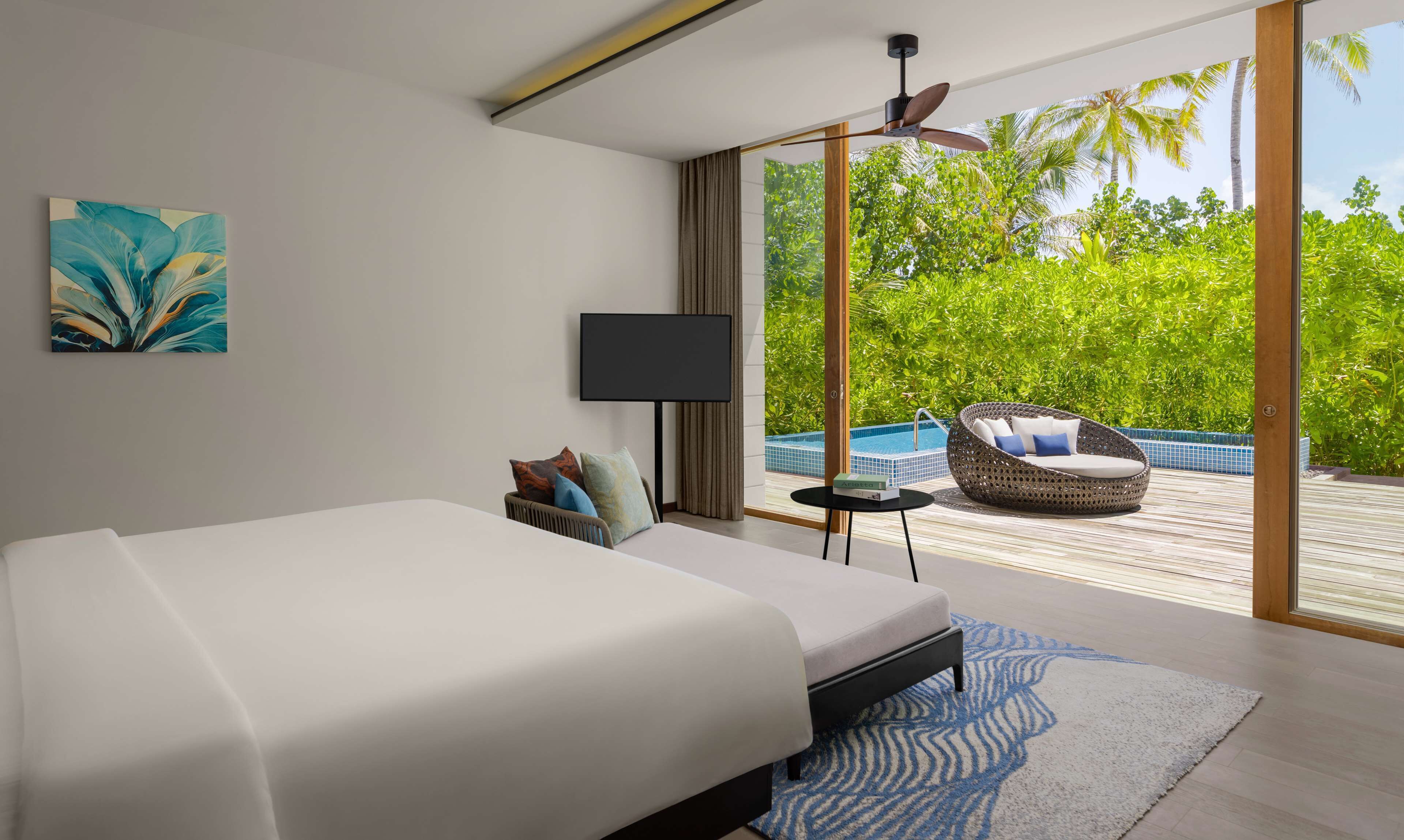 Ein modernes Schlafzimmer mit einem großen Bett, einem Flachbildfernseher und Blick auf einen Pool sowie üppiges Grün.