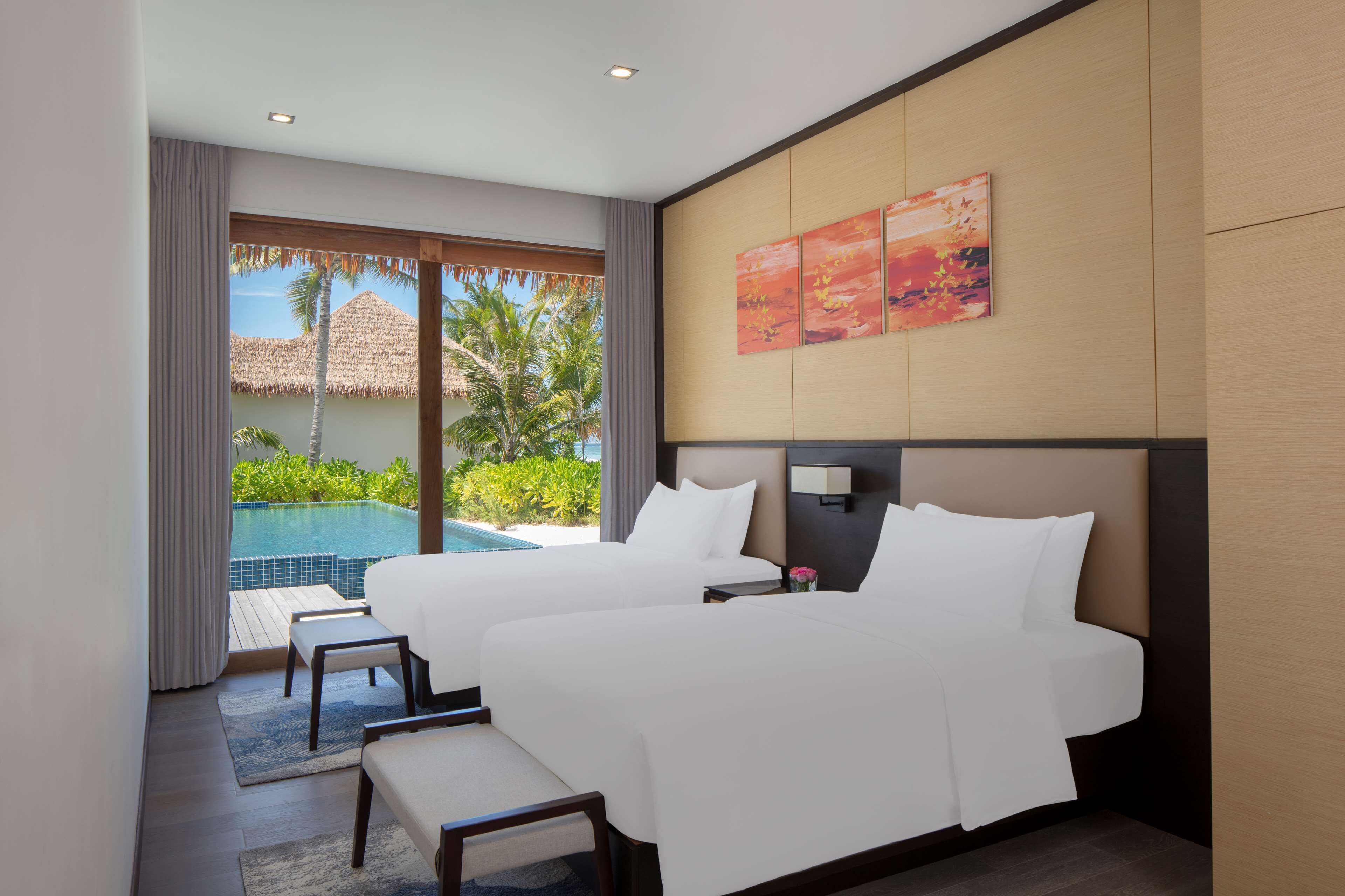 Habitación de hotel con dos camas, un ventanal con vista a una piscina y palmeras, y un cuadro en la pared.