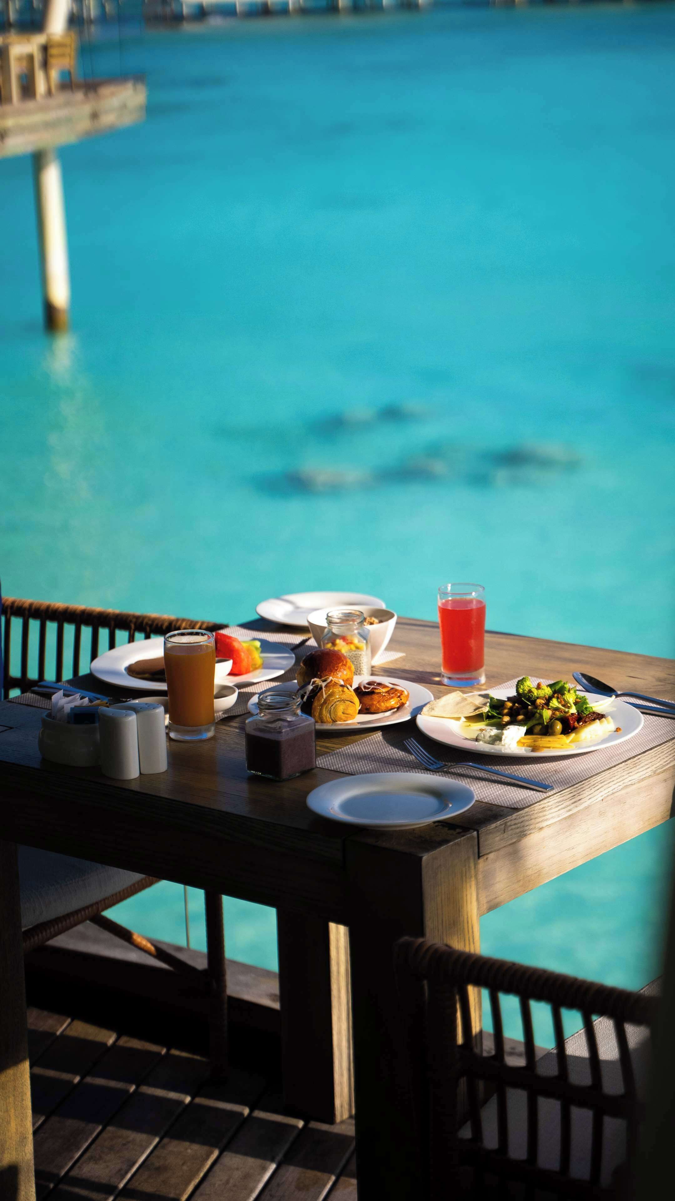 A dining table with breakfast items and a glass of red juice by a pool.