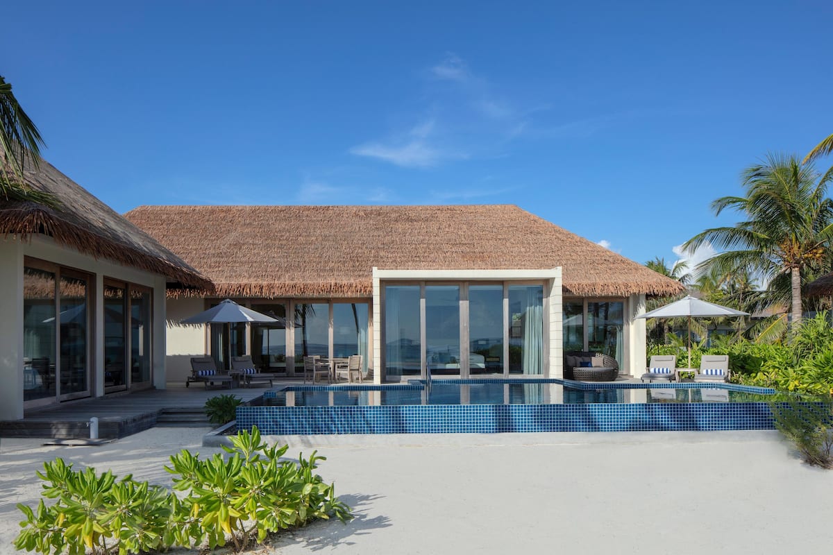 Un resort moderno con piscina, construcciones de techo de paja y zonas de estar al aire libre.