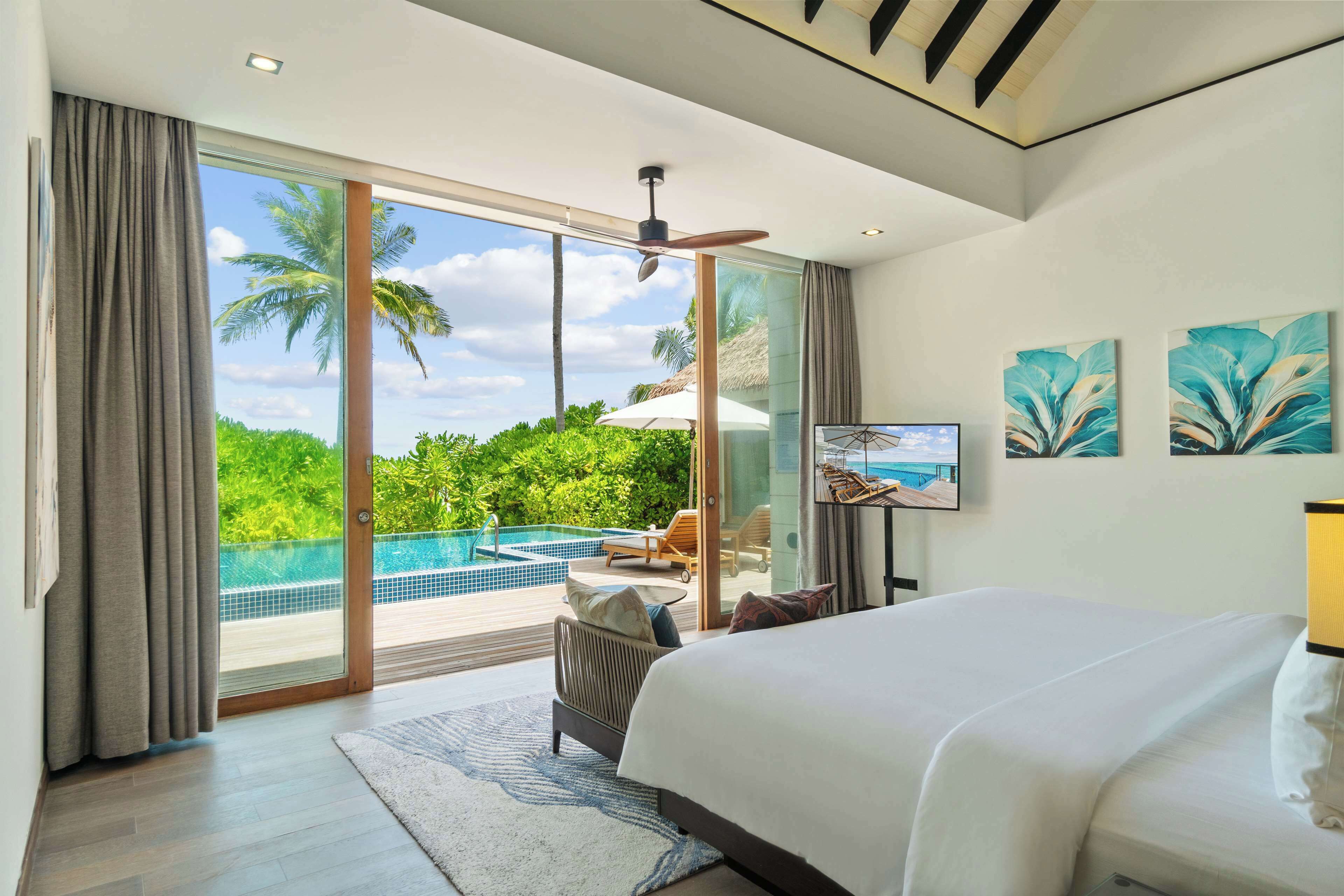 Ein Schlafzimmer mit einem großen Bett, einem Fernseher und Blick auf einen Swimmingpool und Palmen.