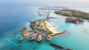 An aerial view of a resort with overwater bungalows connected by walkways, a beach, and a clear blue sea. - Radisson Blu Resort Maldives with 50 percent off on Sea Plane round trip 03 nights & above (Huruelhi Island)