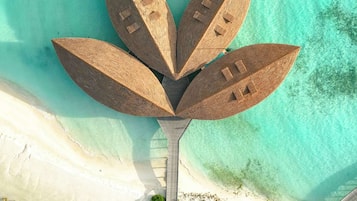 An aerial view of a resort with a central structure resembling a palm tree, surrounded by clear turquoise waters and white sandy beaches.