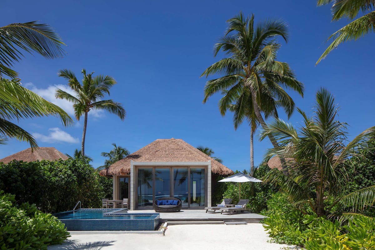 Un resort con piscina, sillones de descanso y estructuras de techo de paja.