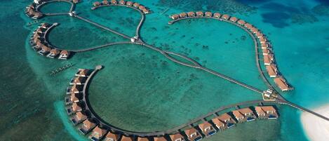An aerial view of a resort with a crescent-shaped layout, connected by a central pier, surrounded by turquoise waters.
