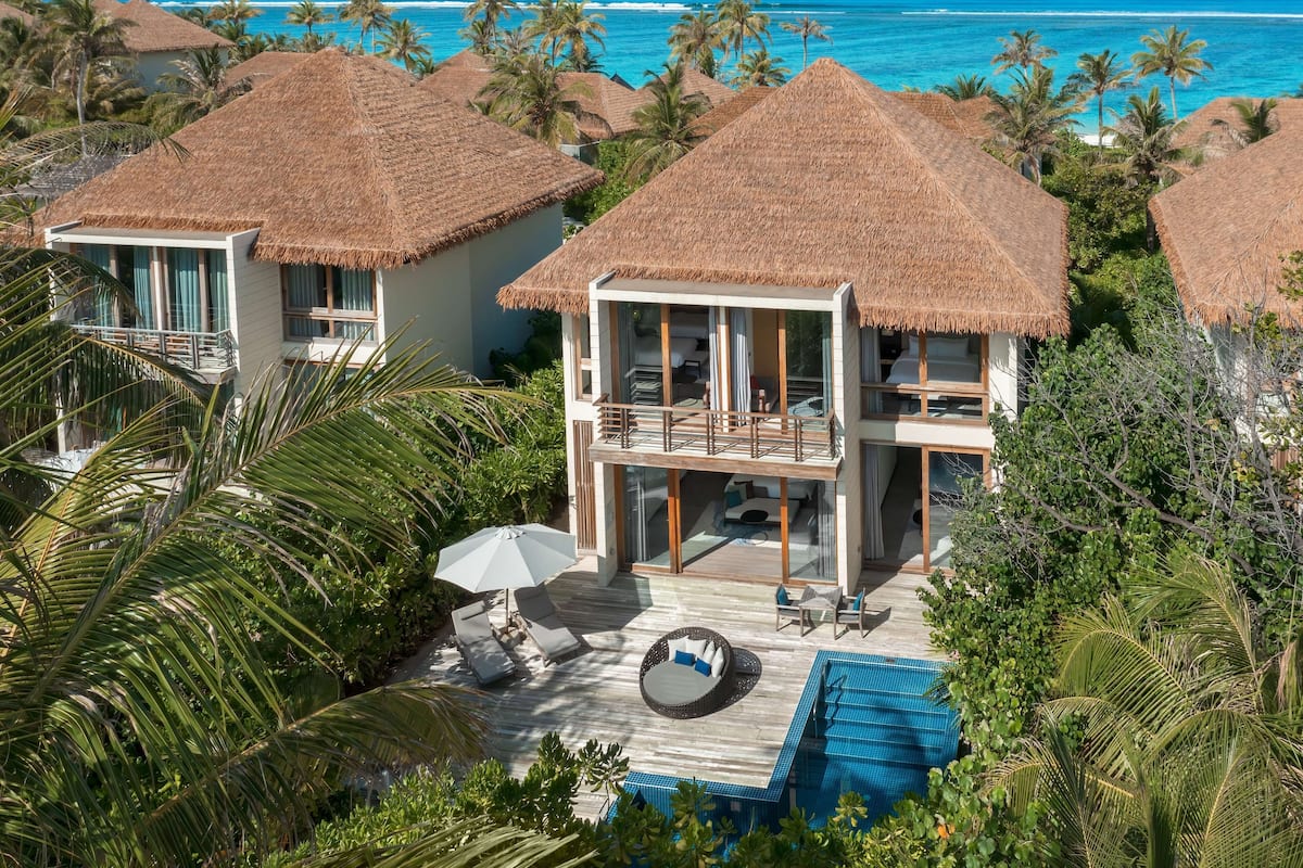 Un resort con bungalows de techo de paja, piscina y vista al océano.