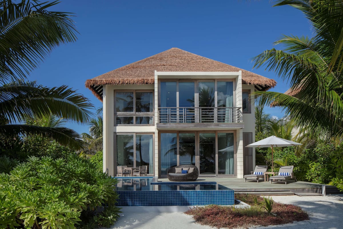 Una casa moderna de dos pisos con un balcón grande, piscina y exuberante vegetación tropical.