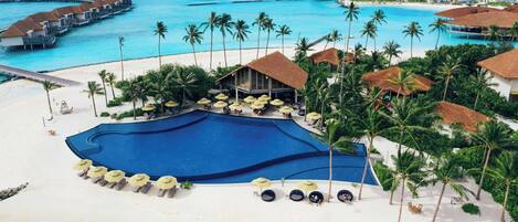 A resort with overwater bungalows, a swimming pool, and a beach area with sun loungers and umbrellas.