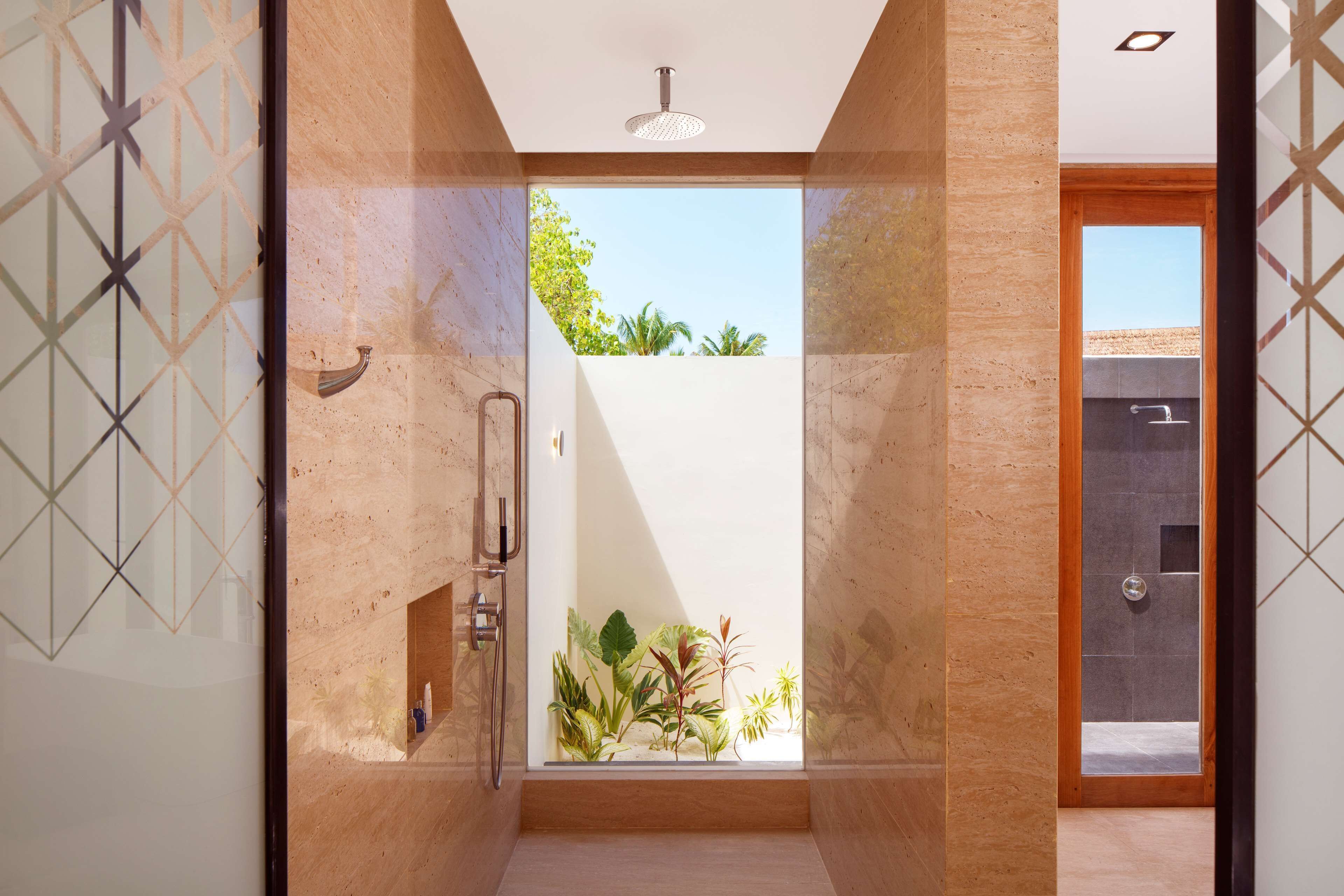 Un baño moderno con ducha, puerta de cristal que da a un balcón con plantas y vistas al cielo.