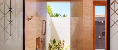 Un baño moderno con ducha, puerta de cristal que da a un balcón con plantas y vistas al cielo.