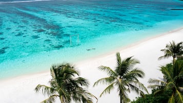 Een strand met helder turquoise water, wit zand en palmbomen.