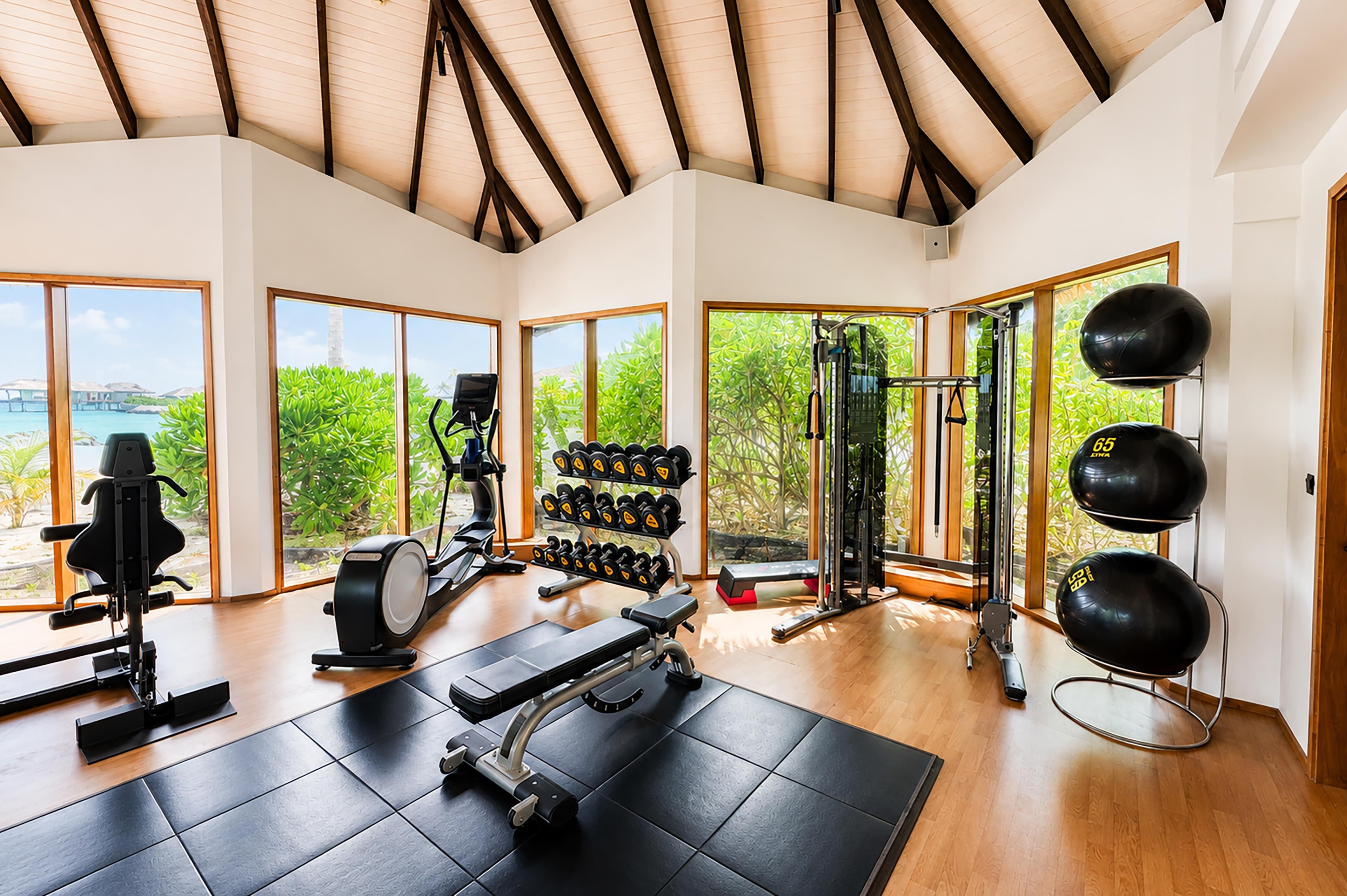 A gym with exercise equipment, large windows, and a view of greenery.