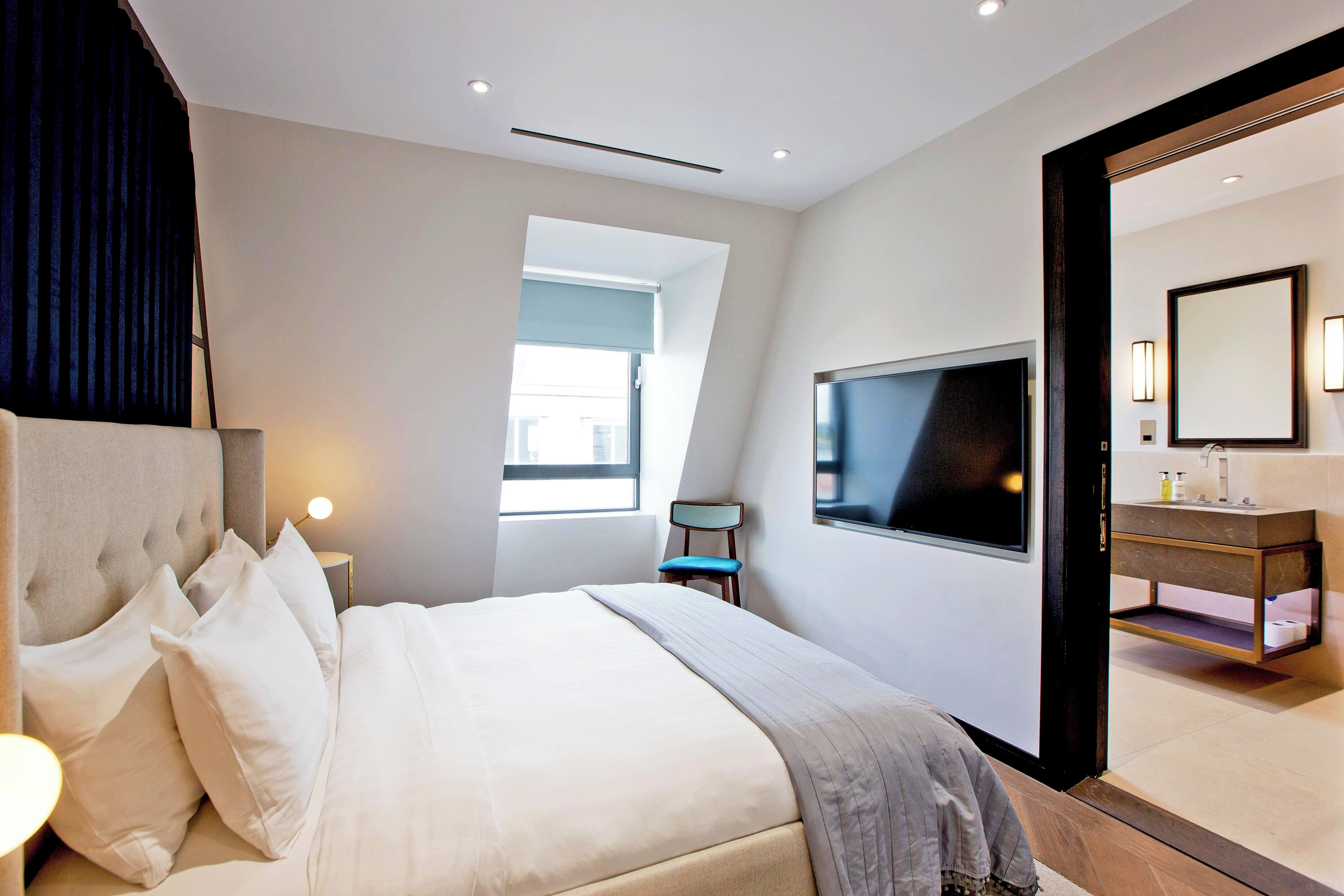 Une chambre d’hôtel moderne dotée d’un grand lit, d’une télévision, d’une salle de bain avec un miroir et d’une fenêtre laissant entrer la lumière naturelle.