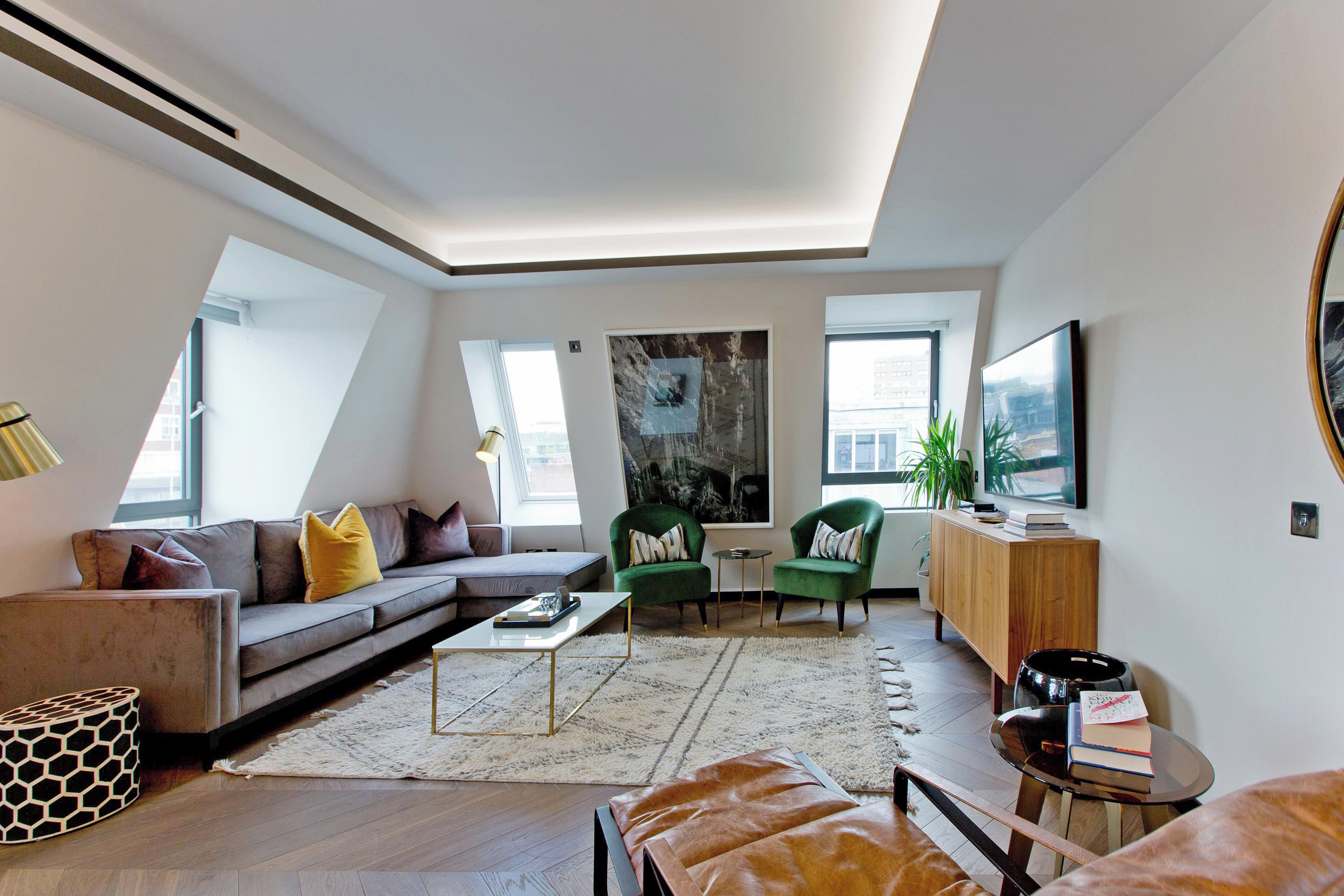A modern living room with a sectional sofa, green armchairs, a coffee table, and a TV.