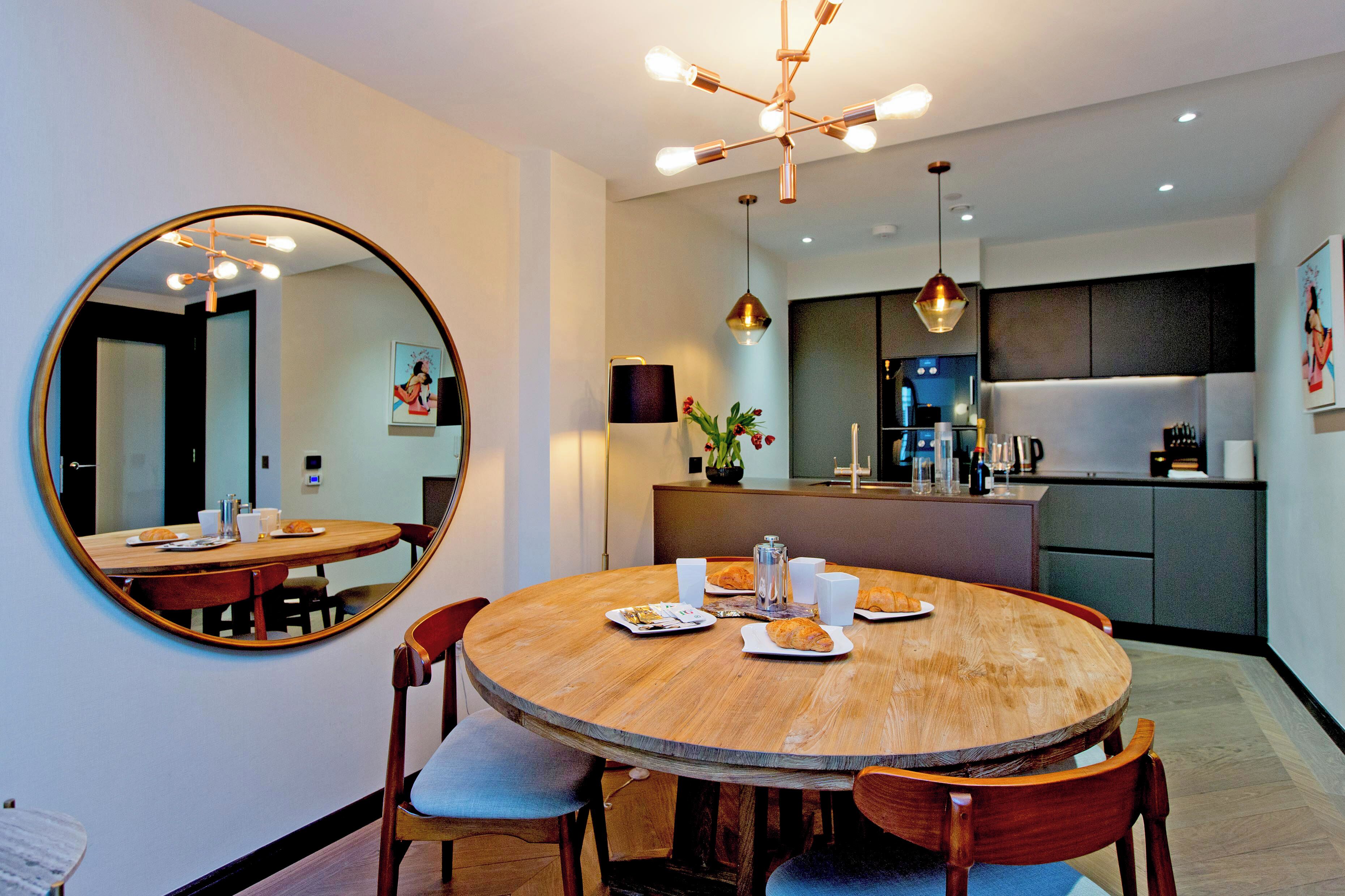 A modern dining area with a round wooden table, chairs, and a large mirror on the wall.