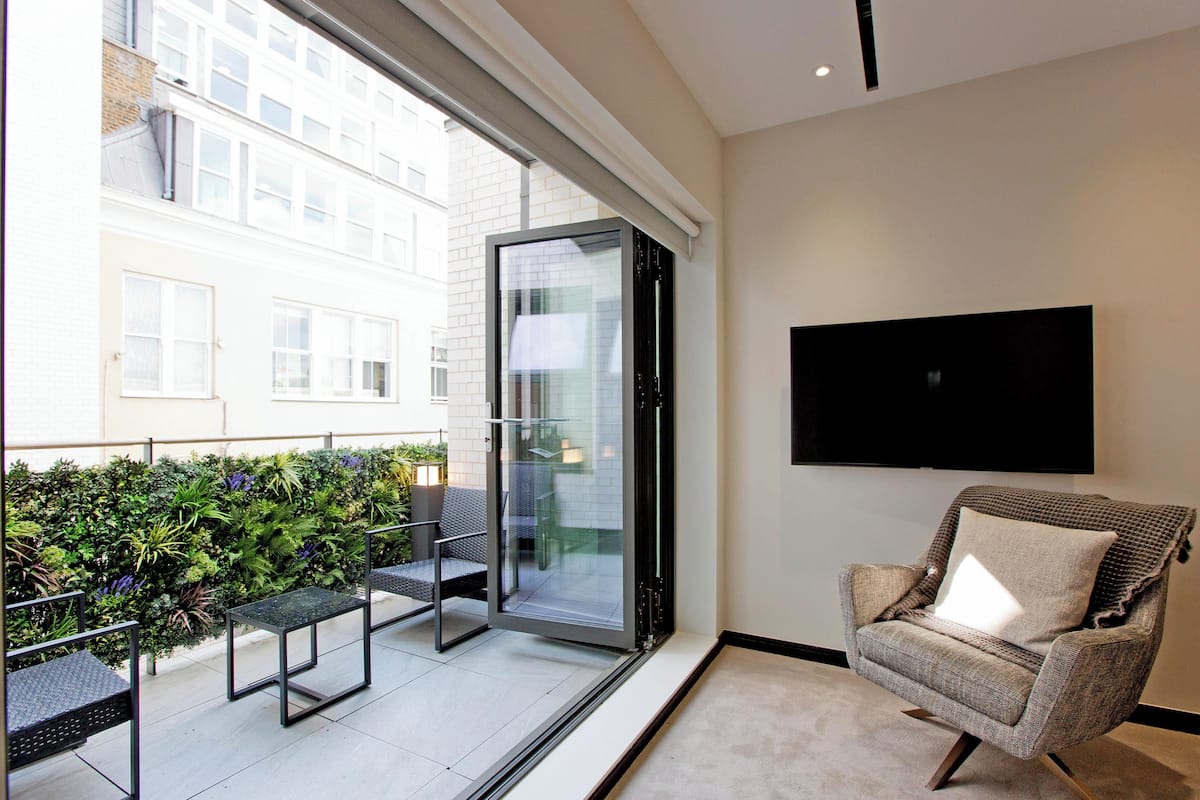 Ein modernes Wohnzimmer mit Glastür zum Balkon, einem wandmontierten Flachbildfernseher und einem bequemen Sessel.