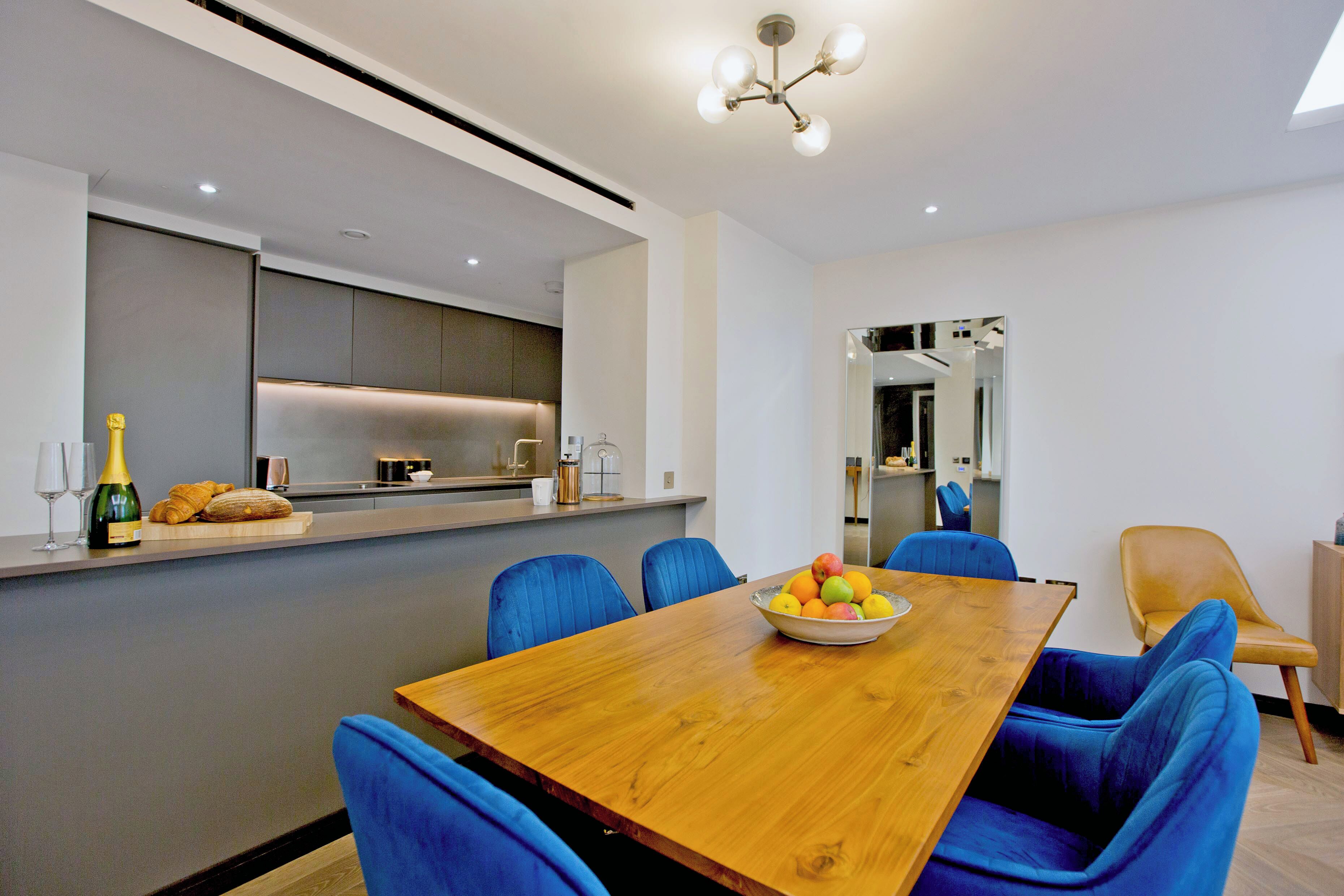 A modern dining area with a wooden table, blue upholstered chairs, and a bowl of fruit.