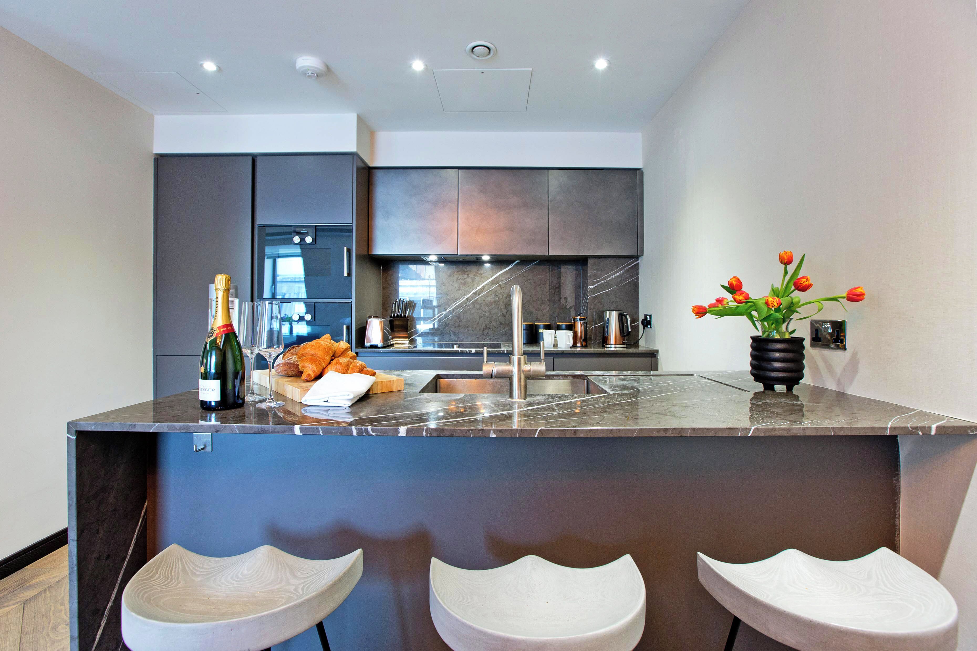 A modern kitchen with a central island, bar stools, a wine bottle, and a vase of flowers.