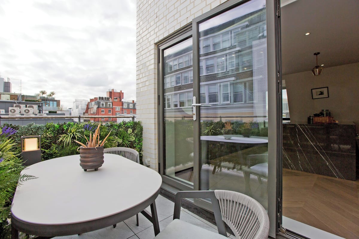 Eine moderne Außenpatio mit einem runden Tisch und Stühlen, einem Blumentopf und Blick auf die Skyline durch große Glasfenster.