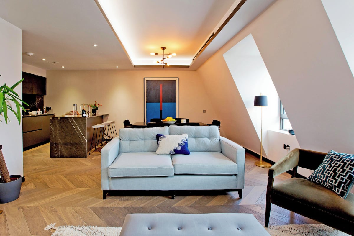 Ein modernes Wohnzimmer mit einem hellblauen Sofa, einem Essbereich und einer Küche im Hintergrund.