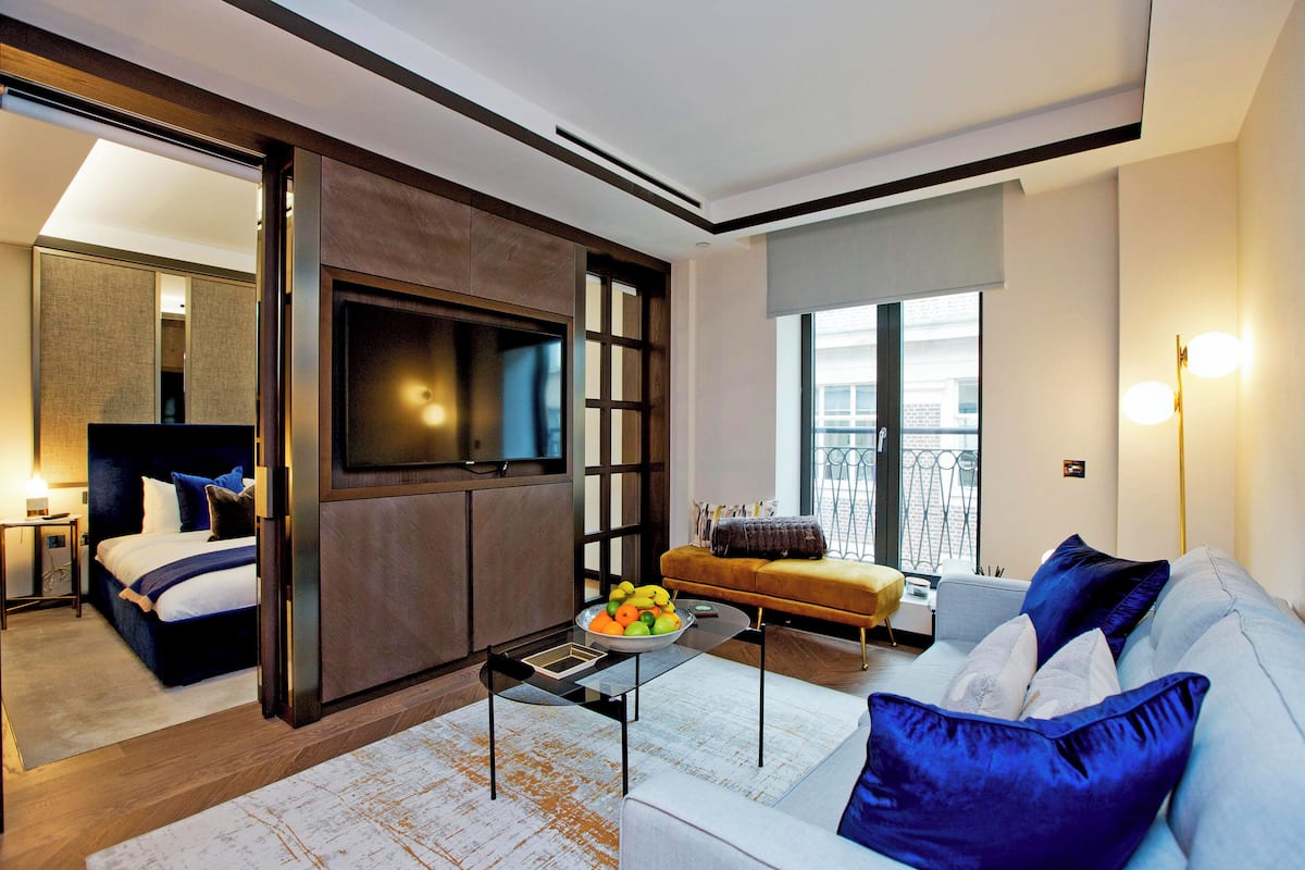 Ein modernes Hotelzimmer mit Bett, Sofa, Couchtisch mit Obst und Fernseher.