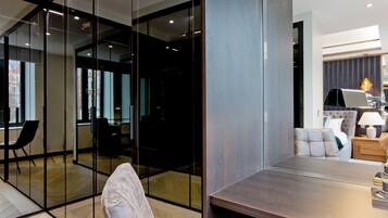 A modern interior with a glass partition, a dining area with a wooden table, and a living space with a sofa and lamp.