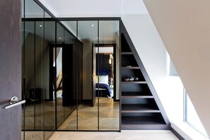 A modern interior with a glass partition, a staircase, and a bed in the background.