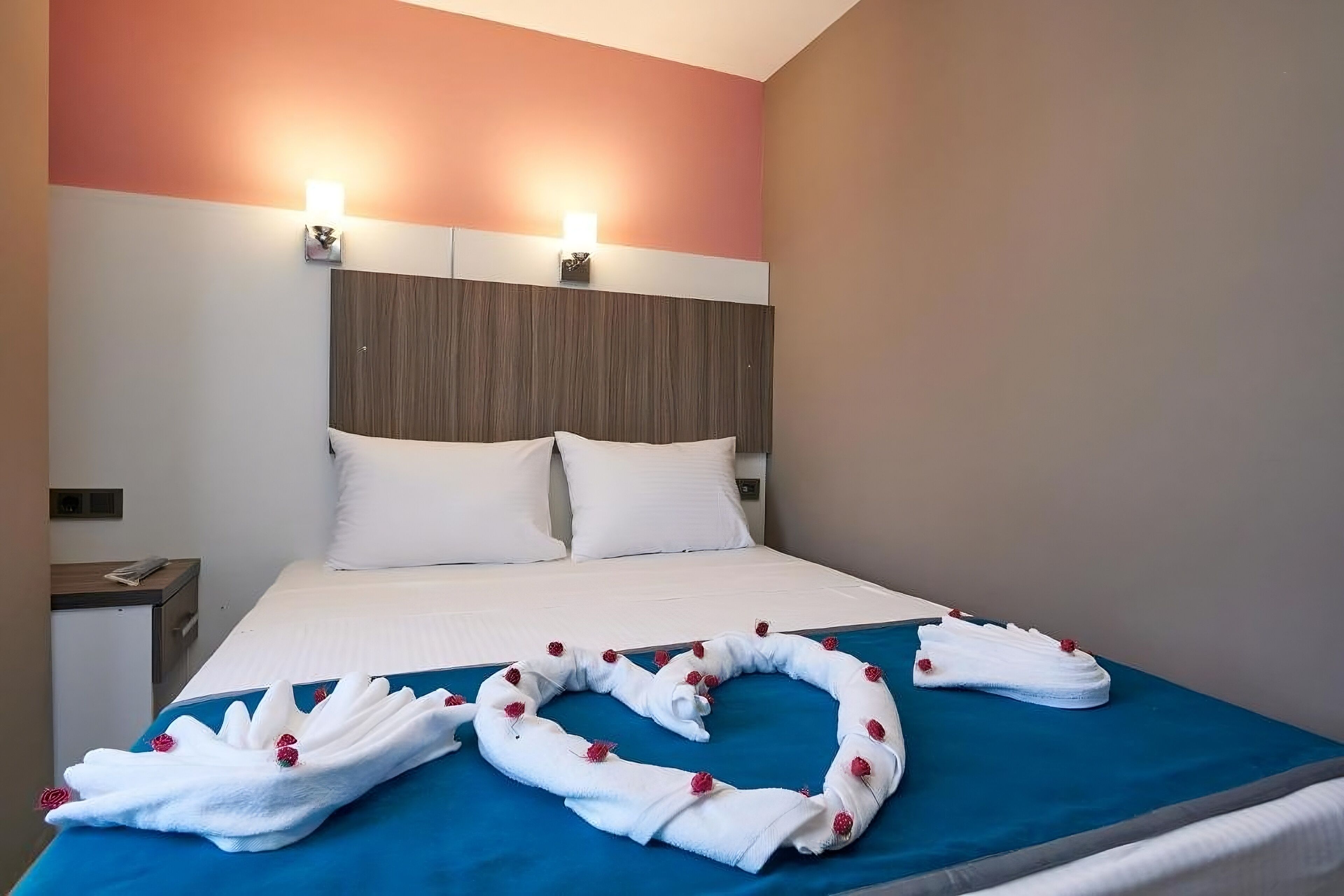 A hotel room with a bed, two bedside lamps, a wooden headboard, and a blue bedspread.