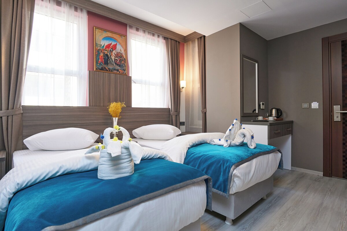 Habitación de hotel con dos camas, un escritorio, un espejo y un cuadro en la pared.