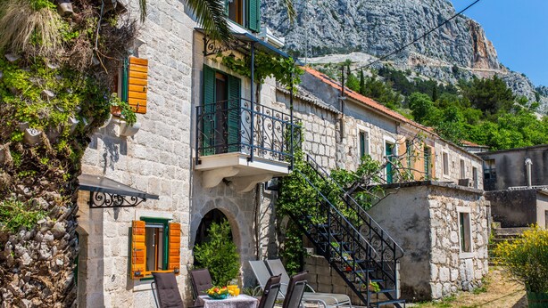 A stone building with a balcony, outdoor seating, and a staircase leading to an upper level. - Holiday house Pivcevi (Podgora)