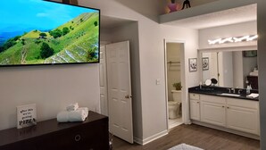 A modern bathroom with a large mirror, vanity, and a television displaying a scenic landscape. - Luxury! 2 king beds and 2 full bathrooms (Manteno)