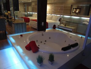 Een moderne badkamer met een groot bad, twee kleine potplanten en rode handdoeken.