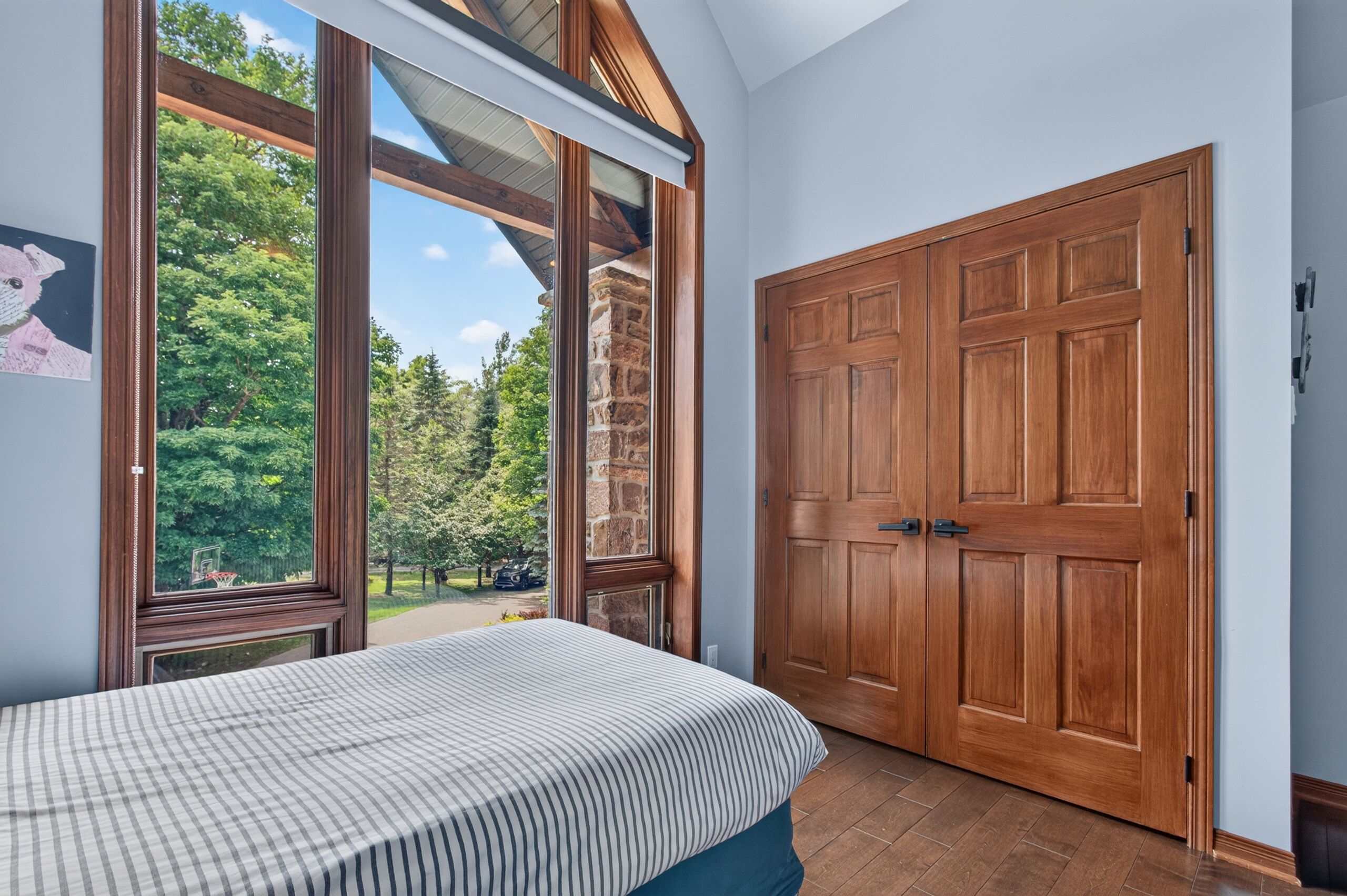 A bedroom with a large window, a bed, and a wooden door.