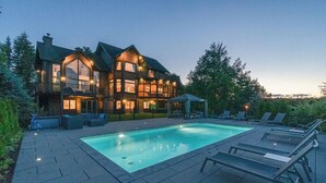 Une grande maison à plusieurs étages, dotée d’une piscine et d’un espace extérieur aménagé pour se détendre.