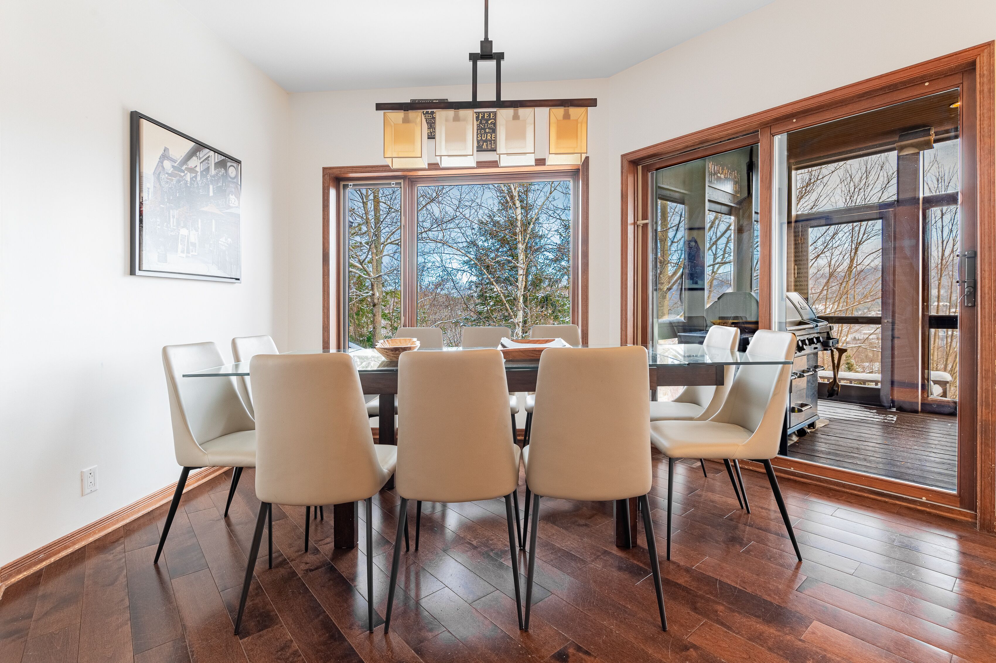 A dining area with a glass table and chairs, large windows, and a view of the outdoors.