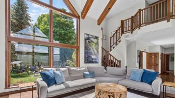 A spacious living room with large windows, a wooden staircase, and a modern design.